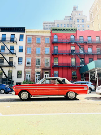 A bright red convertible cruising along a city street on a sunny day.