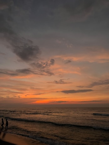 A silhouette of a couple walking along a beach at sunset, the sky painted in warm hues.