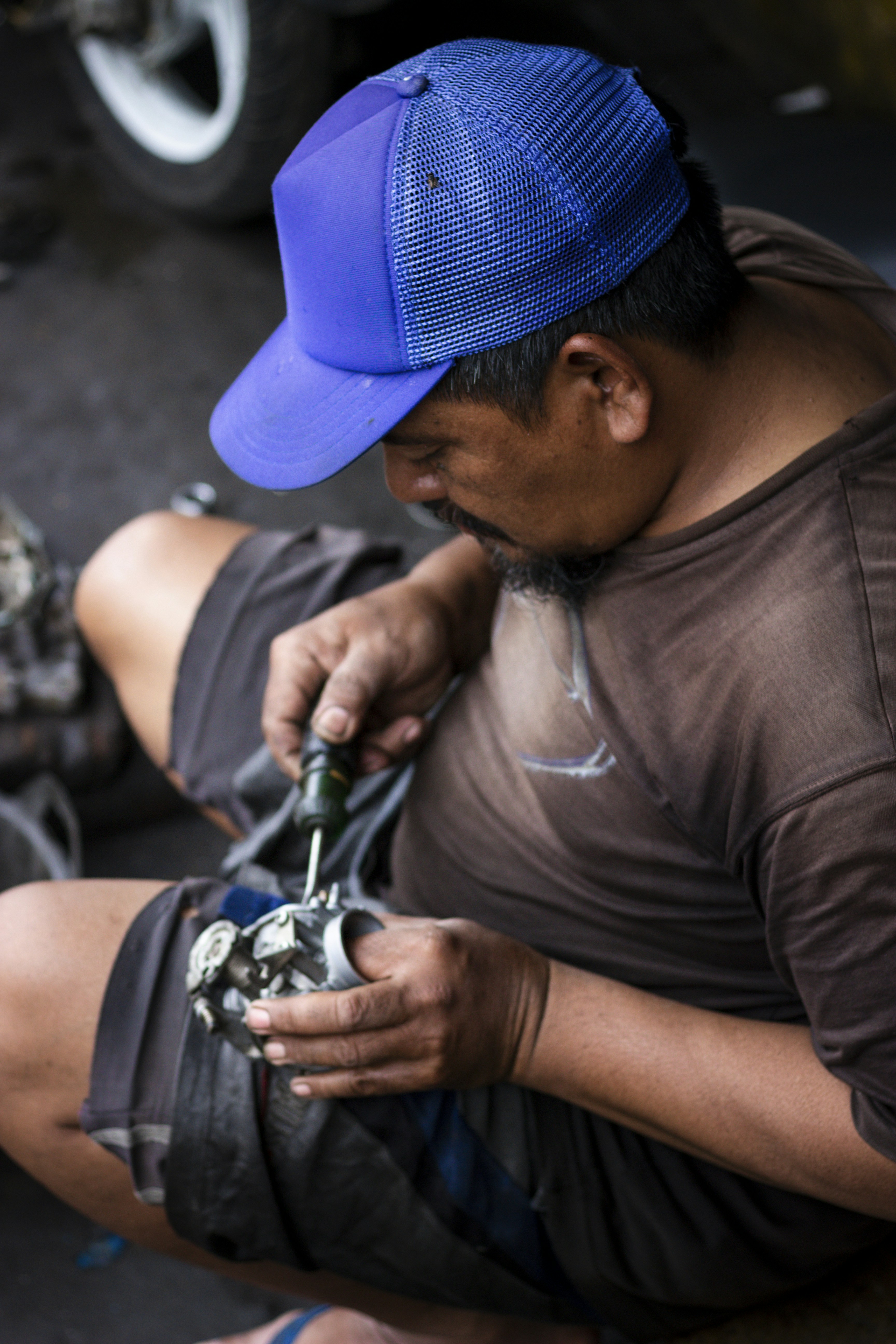 Un homme en casquette bleue répare une pièce moteur avec un tournevis