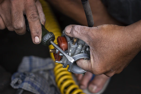 Mechanic's hands repairing a carburetor with a screwdriver.