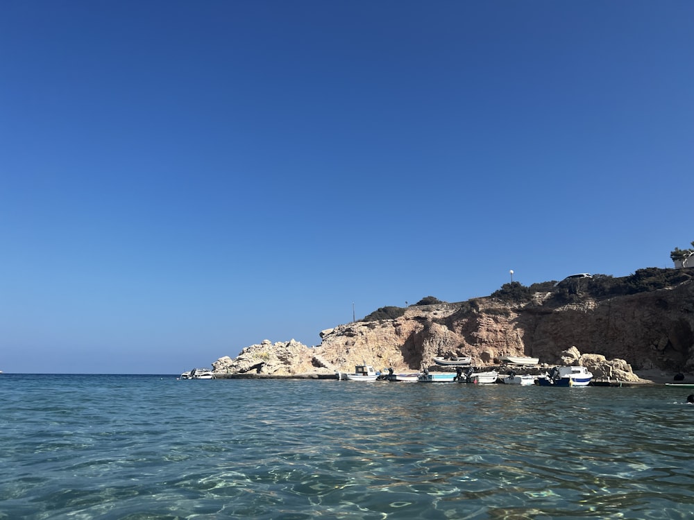 a body of water with boats and a rocky cliff in the background