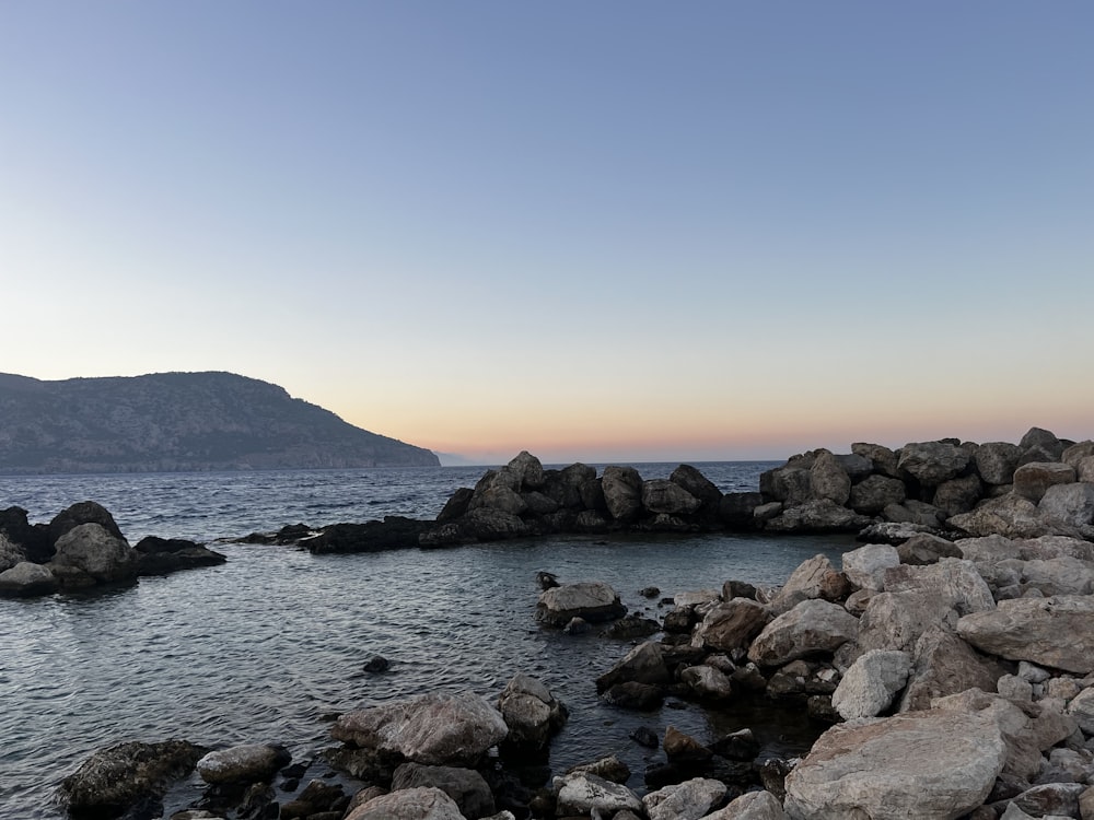 a rocky beach with a body of water and mountains in the background