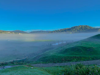 A serene morning view of Neelum Valley with mist rolling over lush green hills.