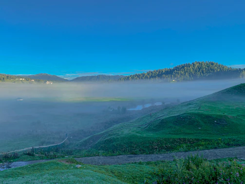 A serene morning view of Neelum Valley with mist rolling over lush green hills.