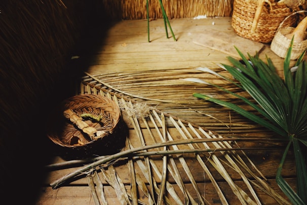 A woven rattan decorative basket filled with fresh greenery on a wooden floor.