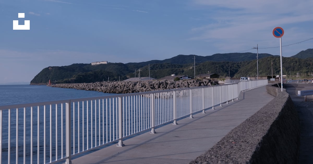 A white railing with a body of water and a hill in the background photo ...