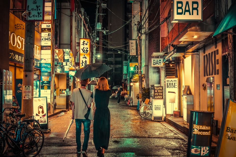 a couple of women walk down a sidewalk under an umbrella