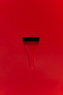 A minimalist design with a bright red surface featuring a subtle groove or indentation. The indentation appears dark, creating a simple yet striking contrast against the red background.