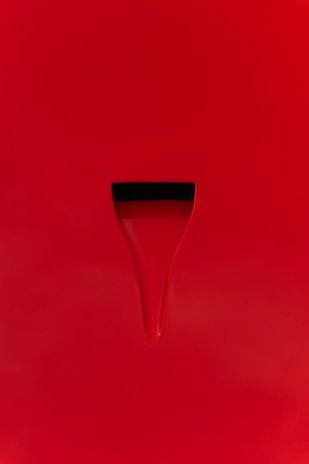 A minimalist design with a bright red surface featuring a subtle groove or indentation. The indentation appears dark, creating a simple yet striking contrast against the red background.