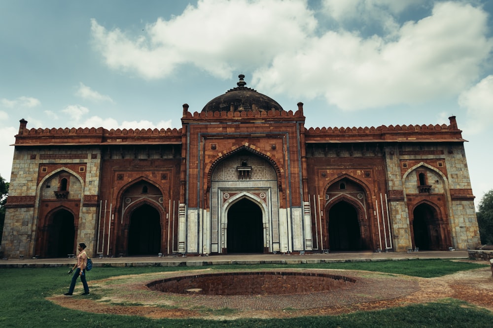 a large building with a person walking in front of it with Purana Qila in the background