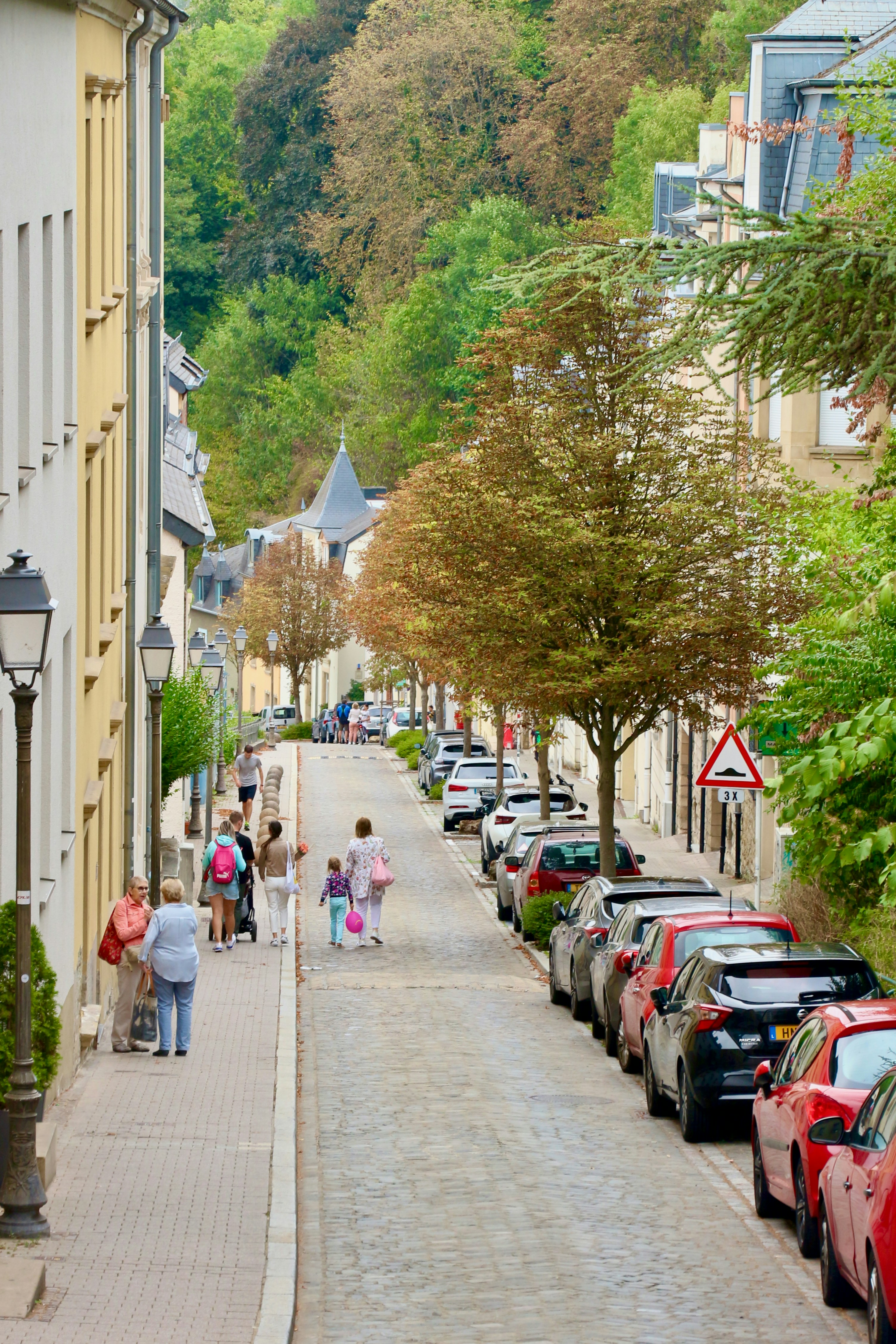 a group of people walking down a sidewalk next to a row of parked cars