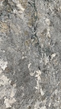 A textured surface with various shades of gray, white, and hints of beige resembling natural stone or rock. It features irregular patterns and speckled areas, giving it a rugged and natural appearance.