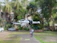 A white drone hovers in the air, captured sharply against a blurred background of trees and buildings. The drone's design features four propellers, and it has a compact, modern appearance with the model name 'MINI 3 PRO' visible on its side.