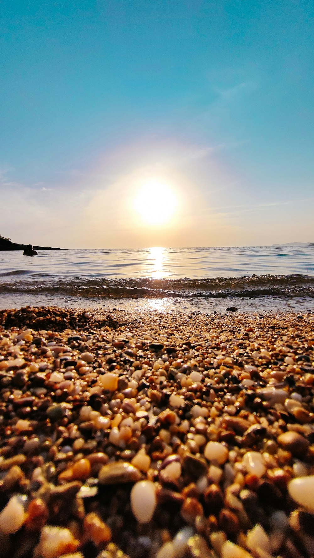 a beach with rocks and the sun in the background