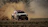 Close-up of a rally driver focused behind the wheel, dust swirling outside the window.