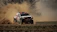 Close-up of a rally driver focused behind the wheel, dust swirling outside the window.
