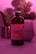 A bottle labeled 'Magic Mushroom Kombucha' is prominently featured, surrounded by a soft, pinkish-purple ambient light. In the background, there is a blurred image of a plant and a glass object, possibly a cup or a vase. The overall scene is moody and uses diffused lighting to create a calming atmosphere.