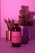 A bottle of Magic Mushroom Kombucha is centered on a surface, illuminated by pink and purple lighting. In the background, there is a glass partially filled with a beverage and two plants, including a cactus, creating a relaxed and modern ambiance.