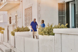 An elderly couple sharing a quiet moment in a sunlit Andalusian courtyard with subtle tech devices in the background.
