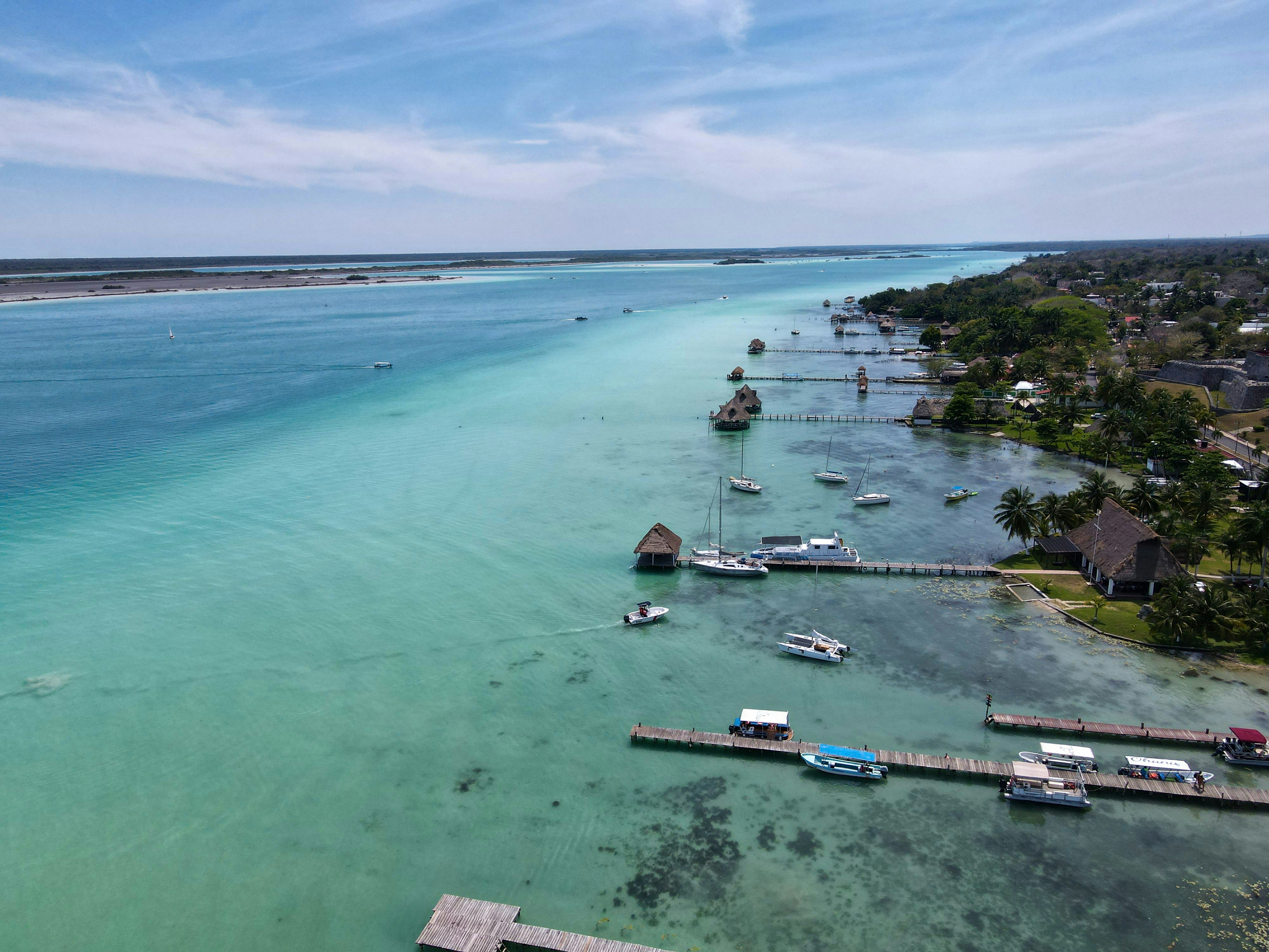 a body of water with boats and buildings along it, A view from above, shot at the majestic Bacalar lagoon, a piece of heaven located at the Yucatan peninsula in southern Mexico.