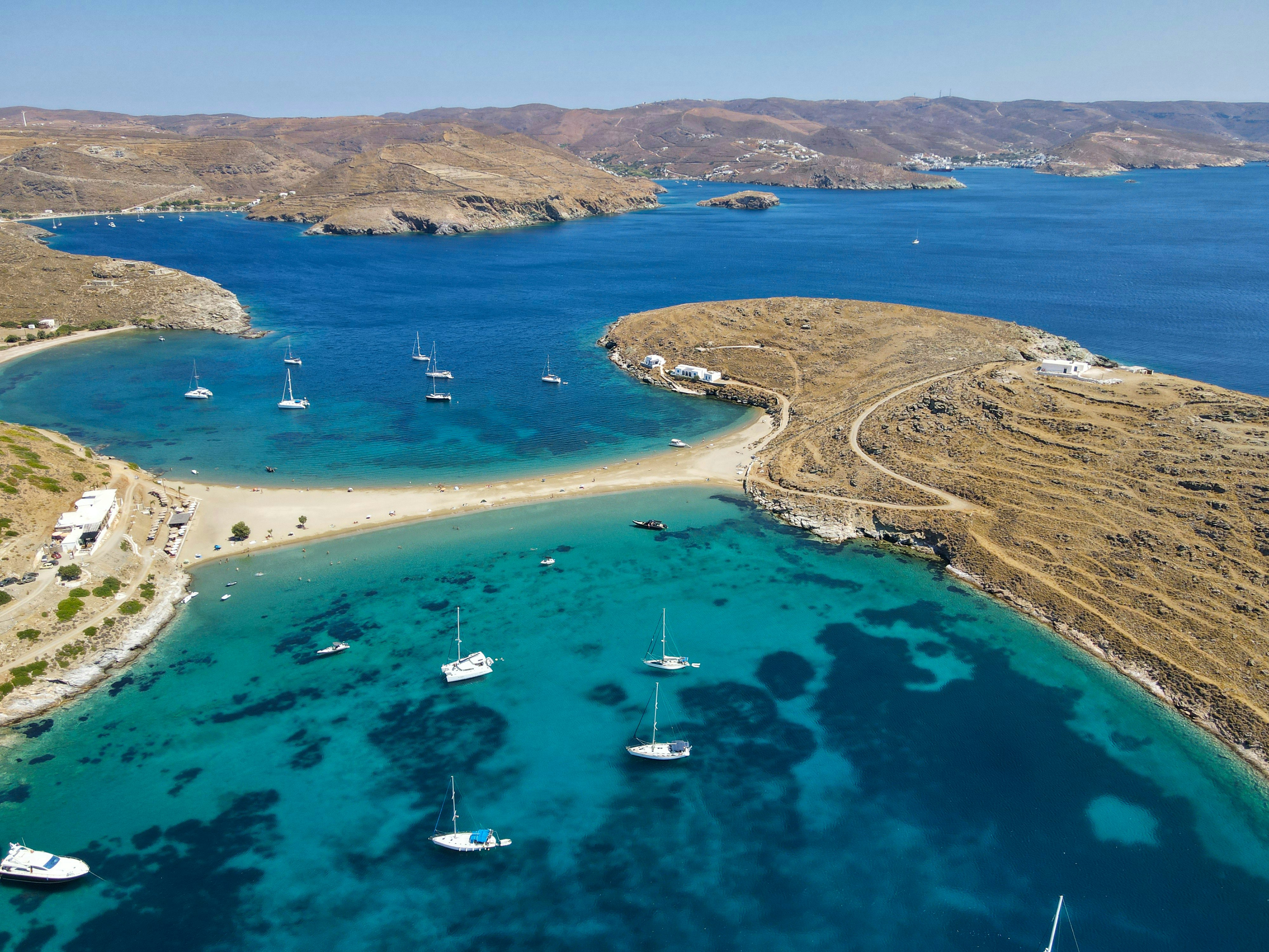 a body of water with boats in it and land around it, A view from above, shot at Kolona beach a famous beach located at Kythnos island in Cyclades, Greece.