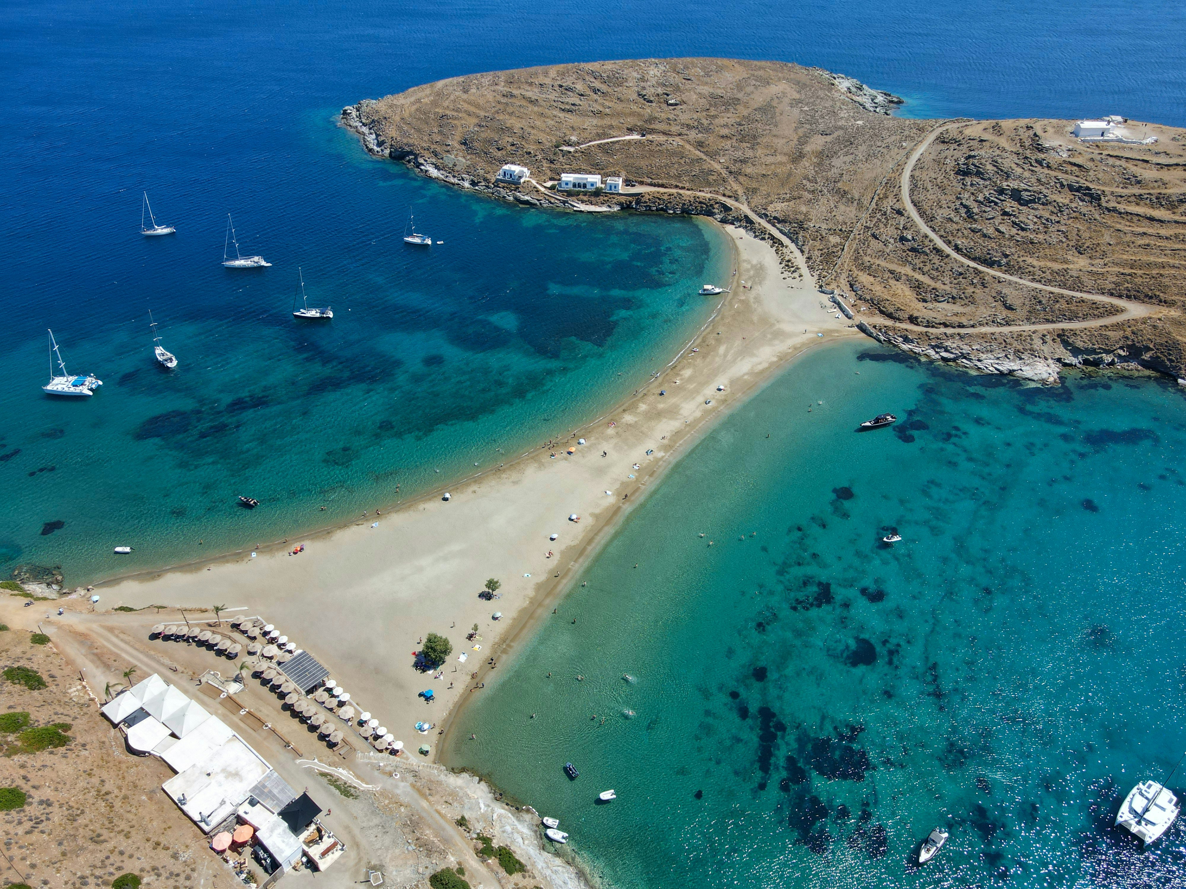 a beach with boats and buildings, A view from above, shot at Kolona beach a famous beach located at Kythnos island in Cyclades, Greece.
