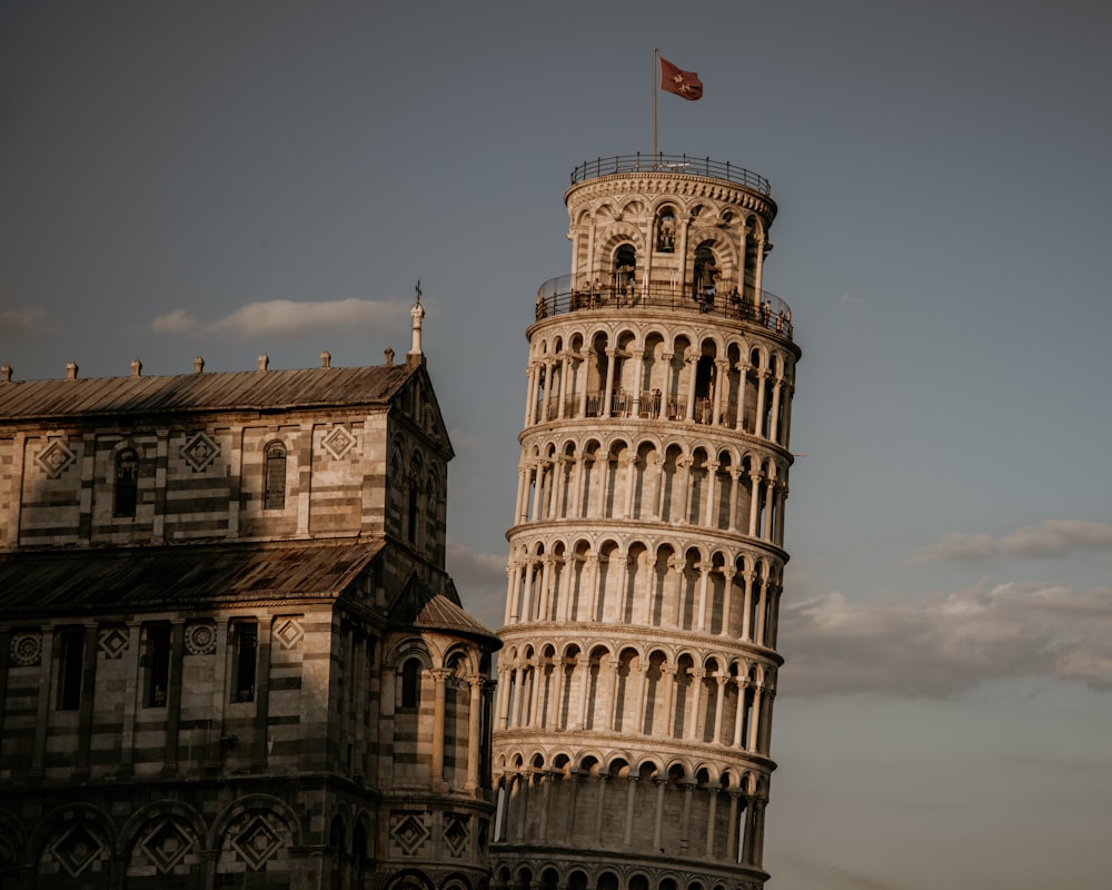 a tall tower with a flag on top with Leaning Tower of Pisa in the background