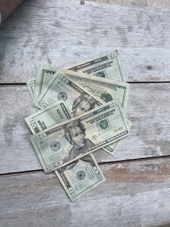 A close-up of hands counting worn dollar bills on a wooden table, symbolizing the real value of money.