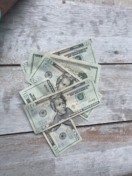 A close-up of hands counting worn dollar bills on a wooden table, symbolizing the real value of money.