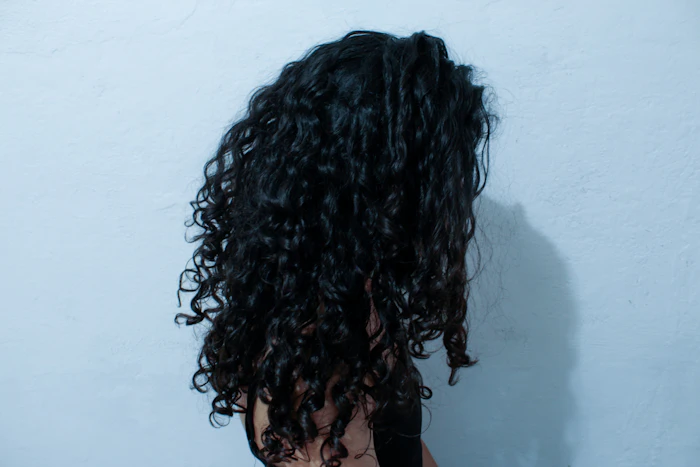 Dark, dense curls seen from behind against a pale wall