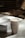 A tall, disposable coffee cup with a sleeve labeled 'coffee bar' is placed on a table with warm, soft lighting. In the background, blurred horizontal slats create a cozy and relaxed cafe atmosphere.