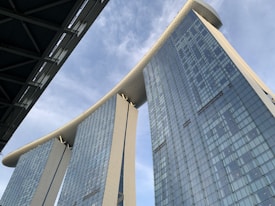 Three modern skyscrapers are connected at the top by a large horizontal structure, resembling a ship, creating a distinctive architectural silhouette against a cloudy sky.