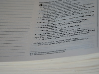 Close-up view of an open book with text printed in a serif font, highlighting several numbered sentences focused on gaining wisdom and knowledge. The page is slightly curved, with a lined margin on one side.