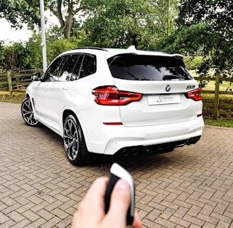 a hand holding a phone in front of a white car