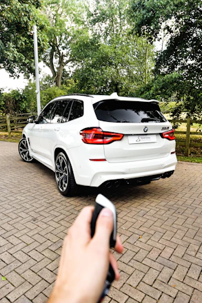 a hand holding a phone in front of a white car