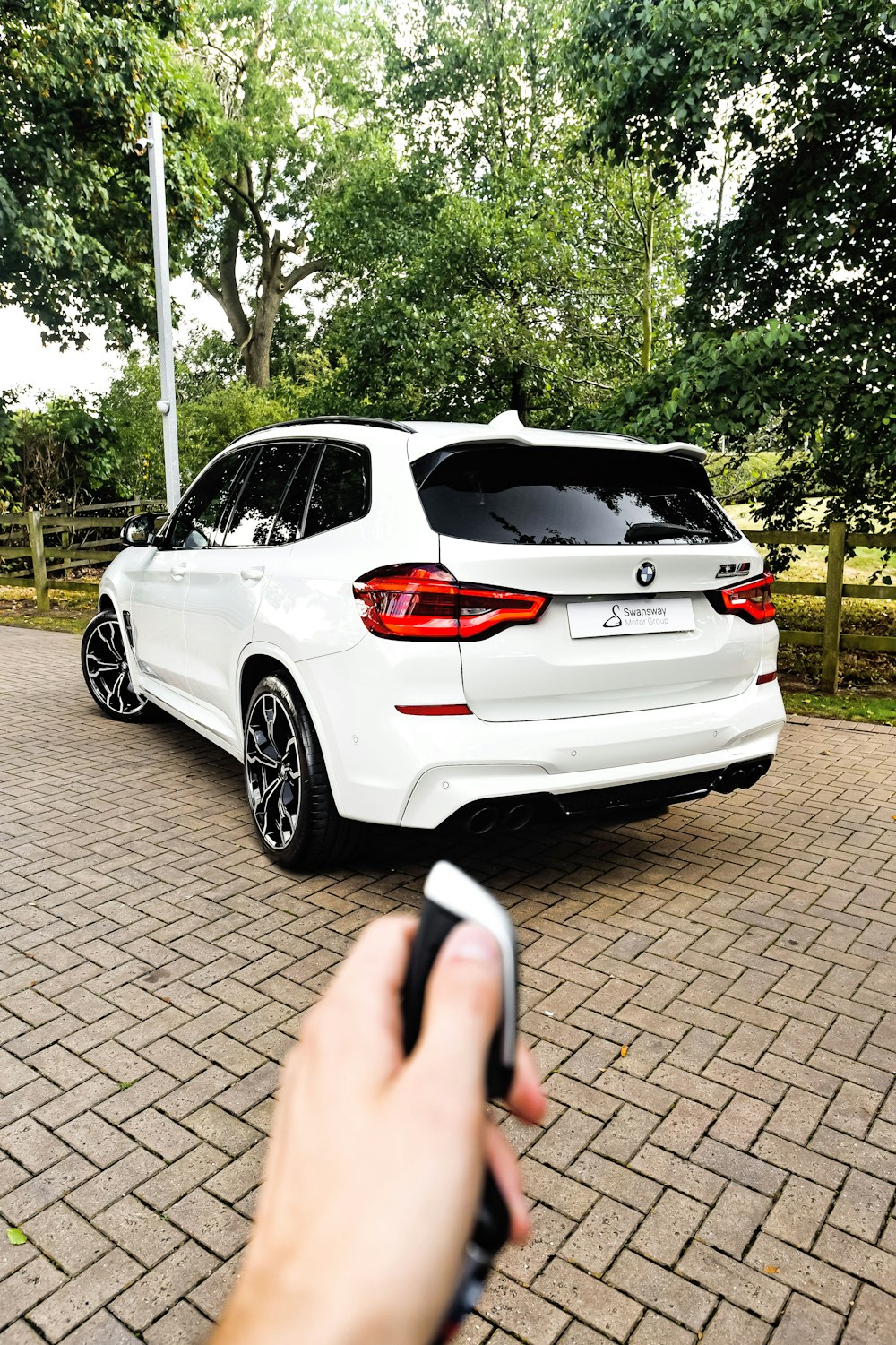 a hand holding a phone in front of a white car