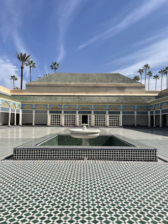 Elegant Moroccan riad courtyard with zellige tiles and palm trees under warm sunlight.