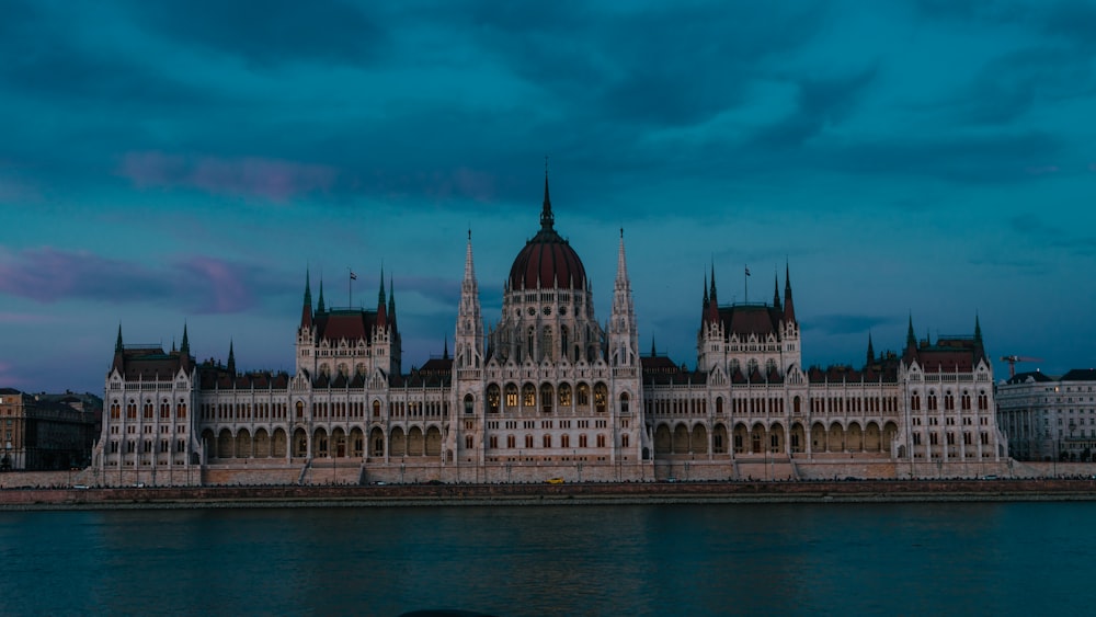 a large building with a domed roof by a body of water with Hungarian Parliament Building in the background