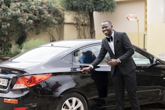 a person in a tuxedo leaning on a car
