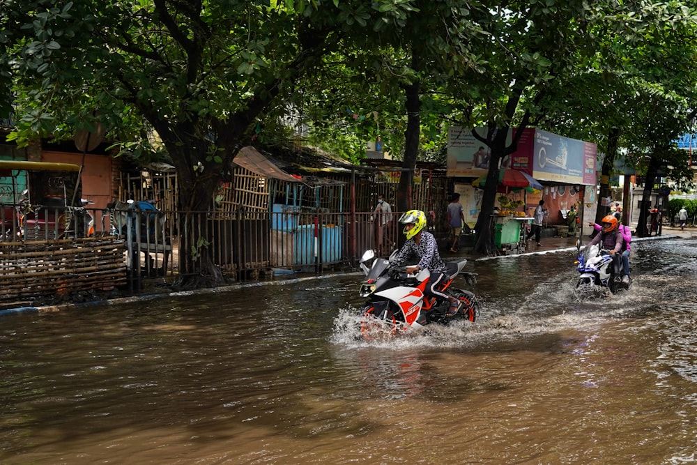um grupo de pessoas andando de motocicleta por uma rua inundada