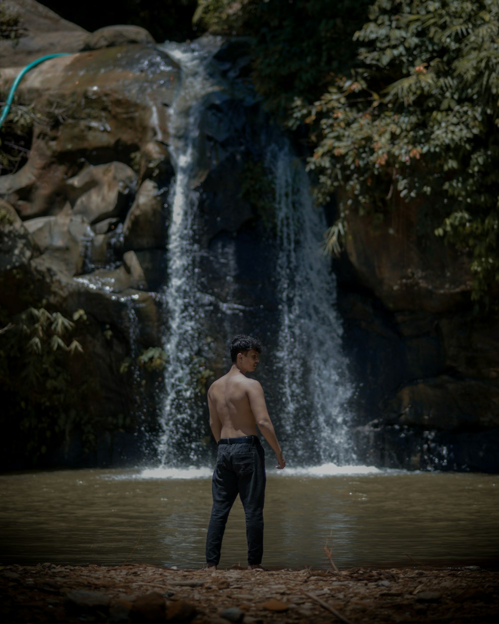 a man standing in water with a waterfall behind him