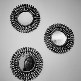 Three round decorative mirrors with intricate beaded frames are mounted on a wall. The bottom mirror reflects part of a person's face, creating a subtle focal point.