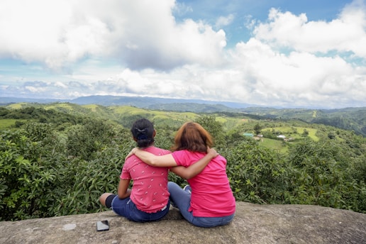 two women sitting on a ledge overlooking a valley