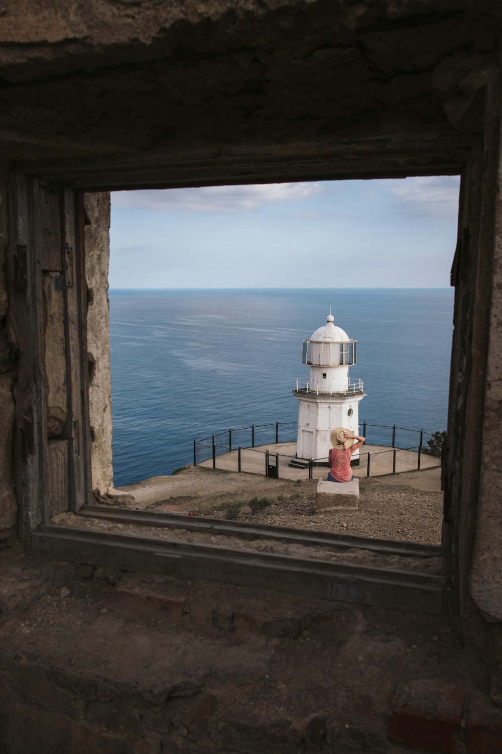 a girl sitting on a bench looking out a window at the ocean