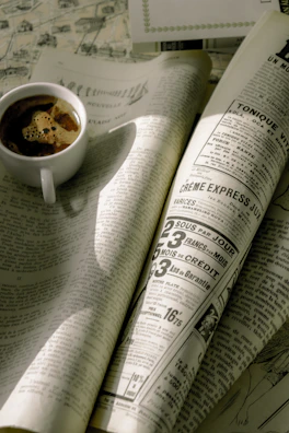 An elegant coffee cup beside an open magazine on a wooden desk.