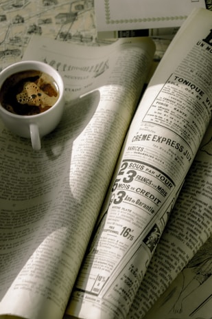 A vintage newspaper spread open on a rustic wooden table with a steaming cup of coffee nearby.