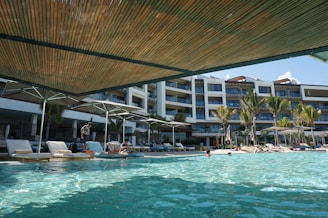 Wide shot of a large hotel pool area, gleaming under the afternoon sun.