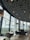 The interior of a modern restaurant with large floor-to-ceiling windows offering a view of a landscape outside. The ceiling is adorned with an artistic design made from overlapping circular tubes. The restaurant features minimalistic furniture, including dark chairs and wooden tables, with soft lighting from hanging lamps.