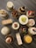 An assortment of intricately decorated pastries and cakes is displayed on a dark, textured surface. Each dessert is uniquely adorned with toppings like fruits, chocolate shavings, and powdered sugar, presented on gold-colored bases.