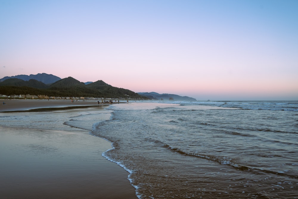 a beach with a body of water and mountains in the background